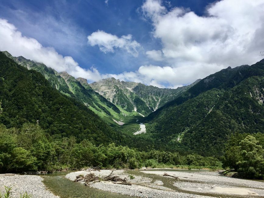 澄み切った青空の下、長野県の緑豊かな山々と川の穏やかな夏の景色。