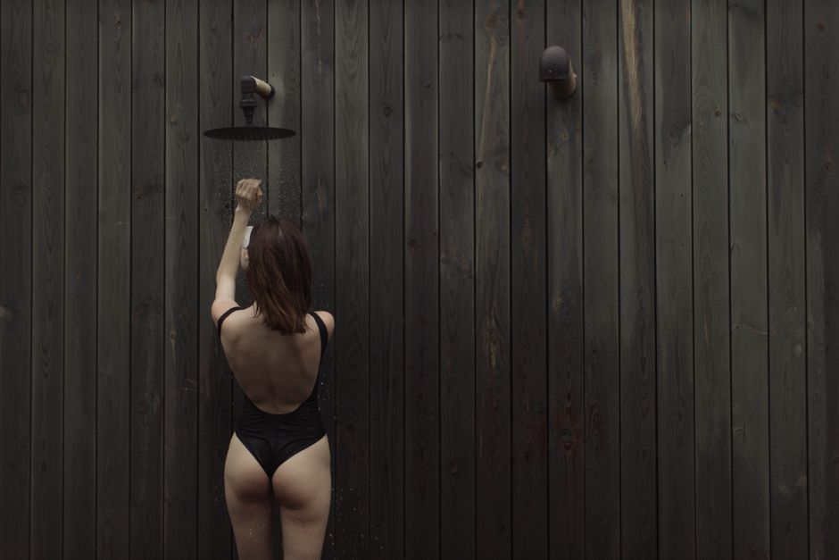木のパネルを背景にした屋外で爽やかなシャワーを楽しむ女性。